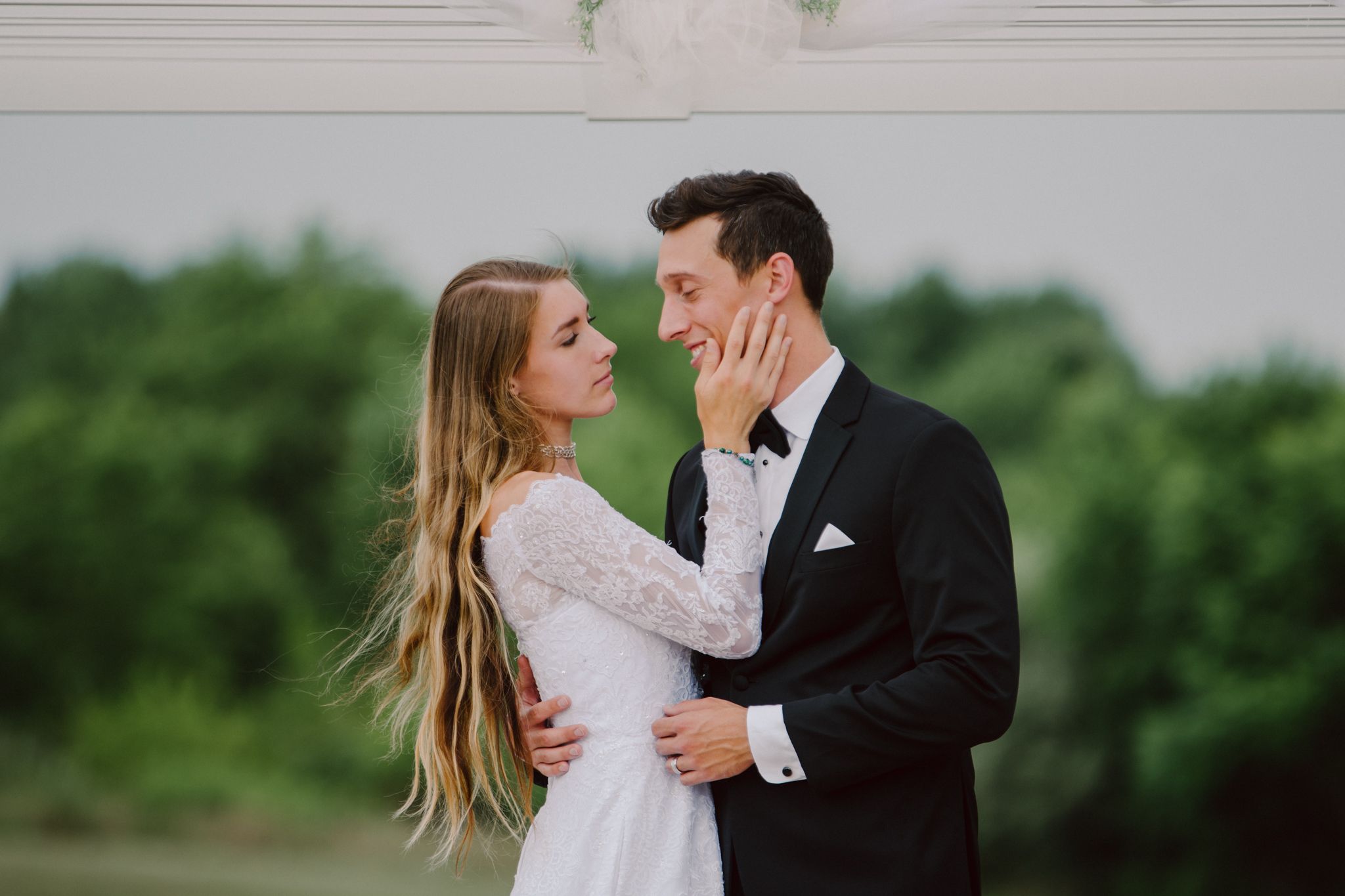 A couple in wedding attire shares an intimate moment in a garden setting with lush greenery in the background