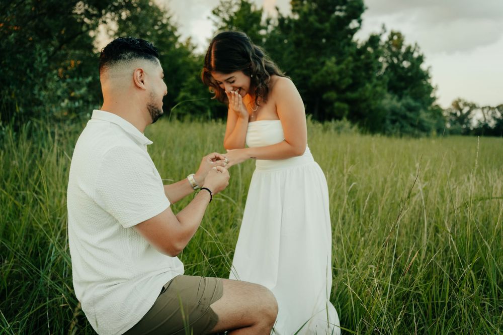 A romantic proposal moment captured in a grassy field with two people in white outfits during golden hour at Manassas battlefield