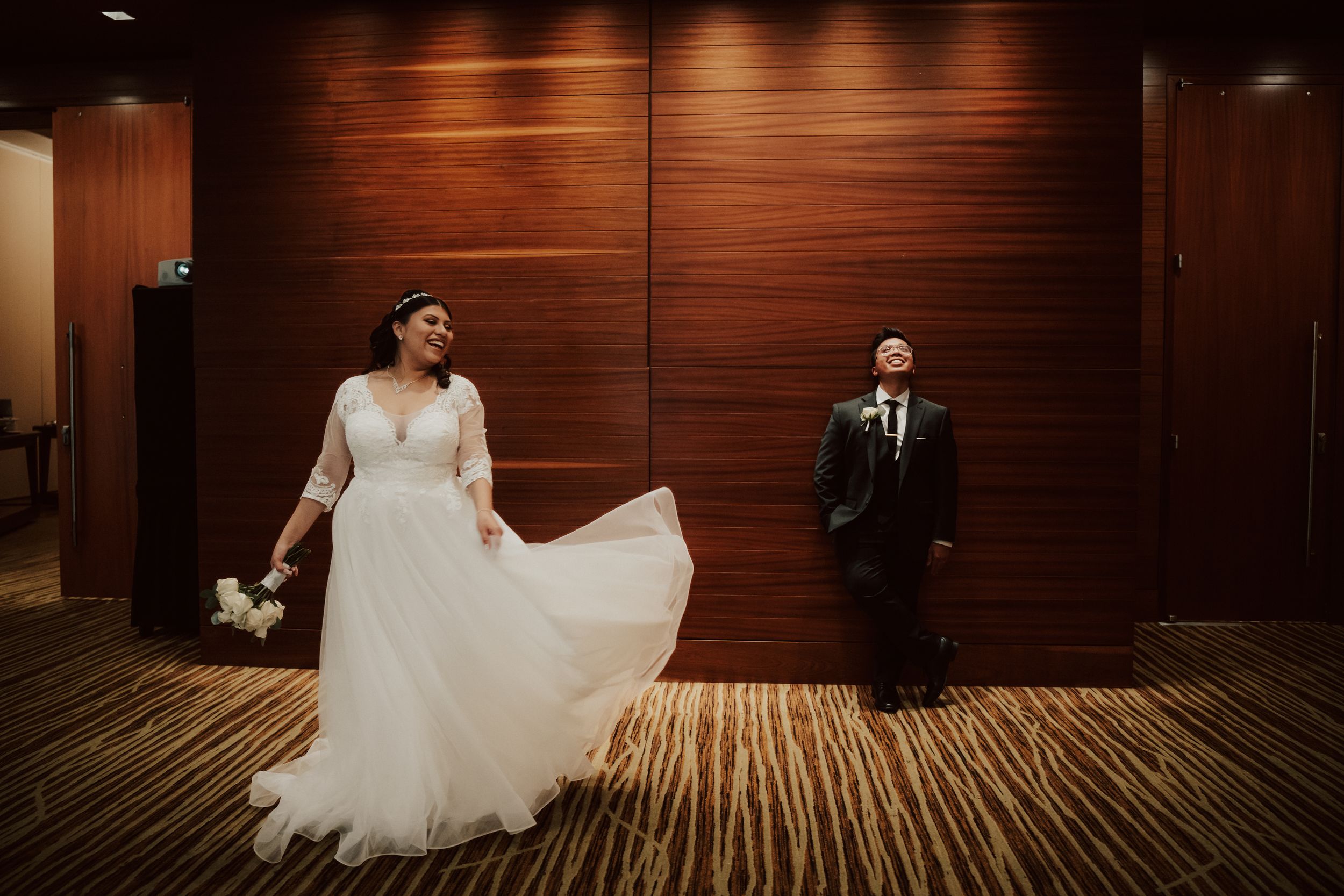 Bride and groom laughing together against a warm wood paneled wall
